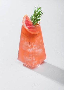 Kırmızı greyfurt kokteyli. Modern lüks bardakta. Meyve dilimi ve beyaz arka planda biberiye. Sert ışık