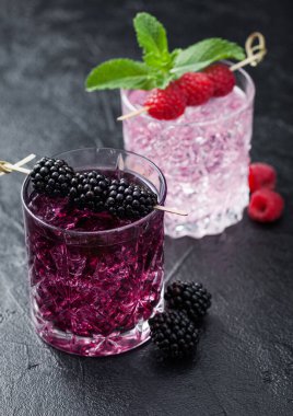 Böğürtlenli yaz kokteyli ve kristal bardaklarda pembe limonata, buz küpleri ve siyah arka planda nane şekeri. Soda ve alkol karışımı. Makro