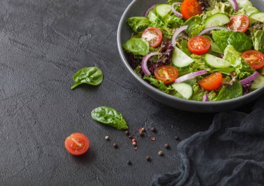 Marul ve domatesli taze sebze salatası, kırmızı soğan ve siyah kâse içinde ıspanak. Mutfak havlusuyla birlikte.