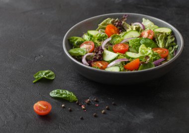 Salatalıklar ve domatesler, kırmızı soğan ve ıspanak taze sebzelerde salata gri kasede salata ve biberli arkaplanda.