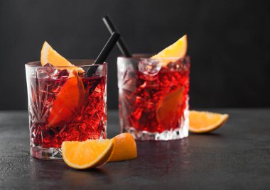 Kristal bardaklarda portakal dilimli Negroni kokteyli ve siyah masa arkaplanlı siyah pipet. Makro