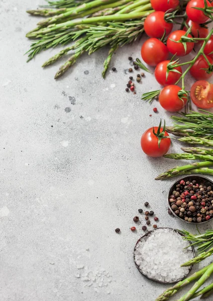 Light food background with healthy organic cherry tomatoes, asparagus and rosemary with bowl of pepper and salt.  Vertical