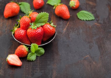 Ahşap masa arkasında çelik kasede yaprak olan organik çiğ çilekler. Metin için boşluk