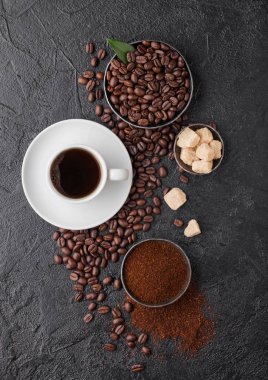 Beyaz fincan taze çiğ organik kahve, fasulye ve kamış şeker küpleri ve koyu arkaplanda kahve ağacı yaprağı. Üst görünüm