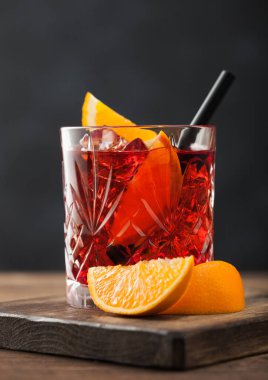 Kristal bardakta portakal dilimli Negroni kokteyli ve ahşap arka planda siyah pipet. Makro