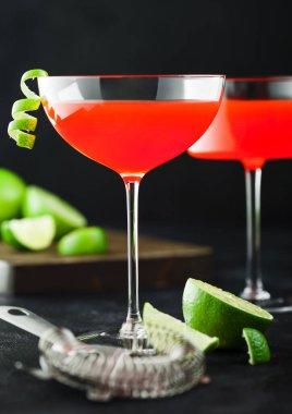 Modern kristal bardaklarda kozmopolitan kokteyli limon kabuğu ve siyah masa arkasında süzgeç ile taze limon..