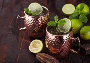 Bakır bardakta Moskova katırı kokteyli, kireç, nane ve ahşap sıkan koyu ahşap masa arkaplanı. Metin için boşluk