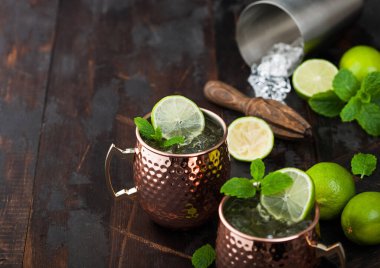 Bakır bardakta Moskova katırı kokteyli, kireç, nane ve ahşap sıkan koyu ahşap masa arkaplanı ve çelik karıştırıcı..