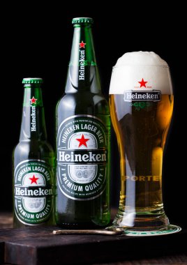 LONDON, İngiltere - 27 Nisan 2018: Koyu ahşap arka planda Heineken Bira şişeleri ve orijinal cam. Heineken, Heineken Enternasyonal 'ın sancak gemisi.