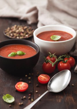 Tahta tahtada çiğ domatesli kaşık, biber ve mutfak beziyle seramik kase kremalı domates çorbası..