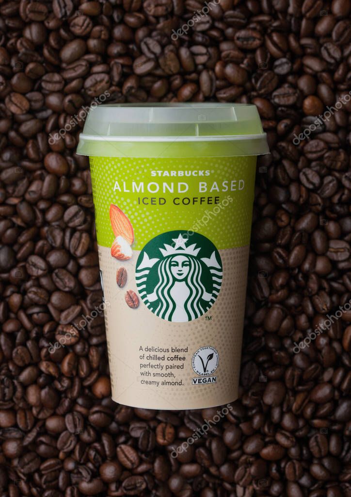LONDON, UK - SEPTEMBER 09, 2020: Paper cup of Starbucks Almond based iced cold coffee on top of fresh raw coffee beans.