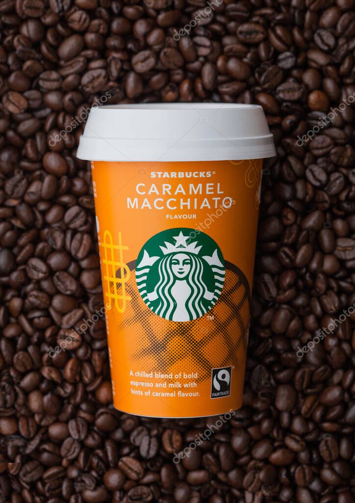 LONDON, UK - SEPTEMBER 09, 2020: Paper cup of Starbucks Caramel Macciato iced cold coffee on top of fresh raw coffee beans.