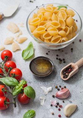 Parmesan peyniri ve domatesli cam kasede taze çiğ koni makarnası, hafif arka planda fesleğenli yağ ve sarımsak. Üst görünüm