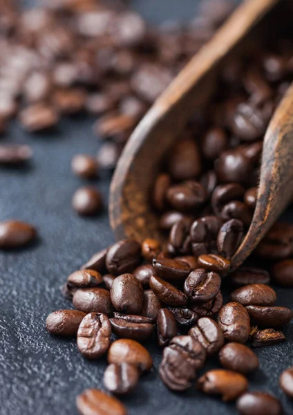 Fresh raw coffee beans in woode scoop on black background. Macro