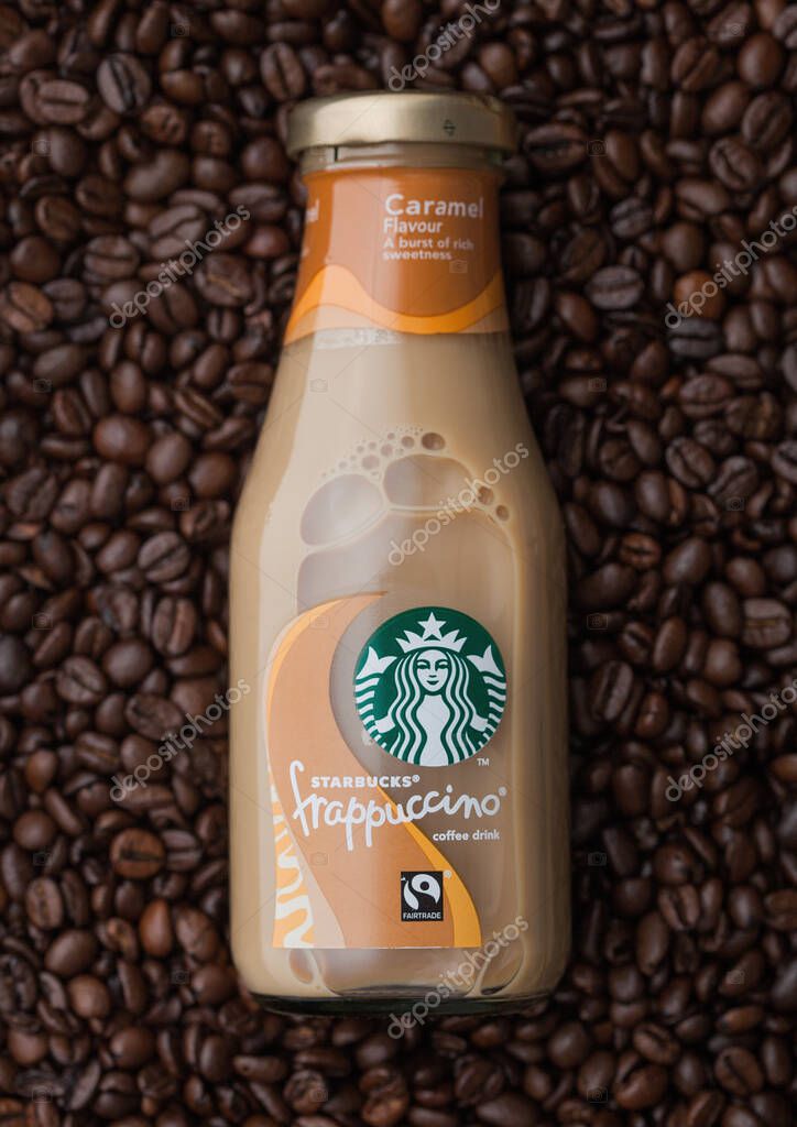 LONDON, UK - SEPTEMBER 09, 2020: Glass bottle of Starbucks frappuccino iced cold coffee on top of fresh raw coffee beans.