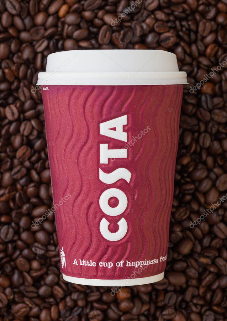 LONDON, UK - SEPTEMBER 09, 2020: Paper cup for takeaway of Costa Coffee on top of fresh raw coffee beans.