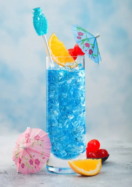 蓝色泻湖夏季鸡尾酒在高球杯与甜鸡尾酒樱桃和橙色片与伞蓝色桌子背景 — 图库照片