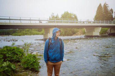 Erkek turist dağ nehrinin yanında duruyor..