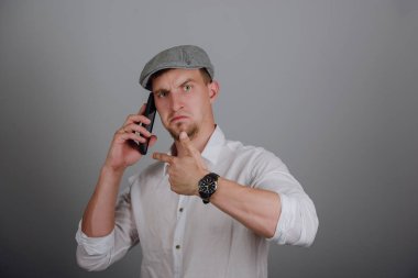 Gri arka planda cep telefonuyla konuşan mutlu genç adamın portresi