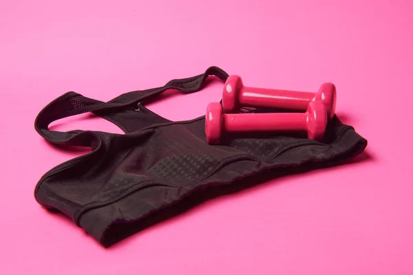 Розовые гантели и черная футболка на розовом фоне — стоковое фото