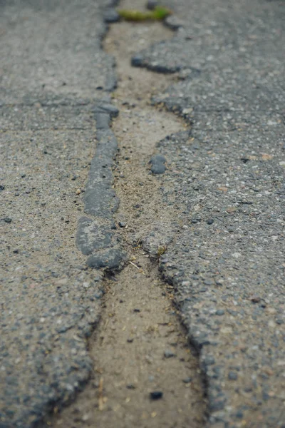 Eine durch Regen und Schnee beschädigte Straße, die instandhaltungsbedürftig ist. Aufgebrochener Asphalt führt zu einem Schlagloch, das für Fahrzeuge gefährlich ist. — Stockfoto