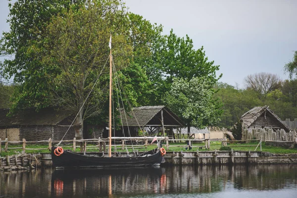 Old wooden viking huts in a village with ship moored at the bank — Stock Photo, Image