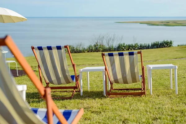 Puste krzesło plażowe na łące w czasie letnim. Światło słoneczne i morze w tle — Zdjęcie stockowe