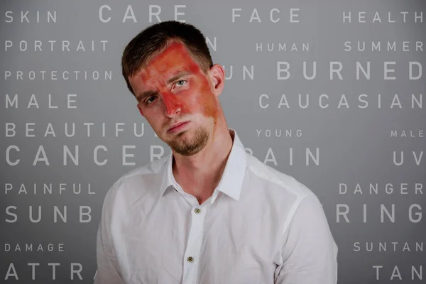 Sad worried indifferent man with a sunburned face. With background made of skin care captions. — Stock Photo, Image