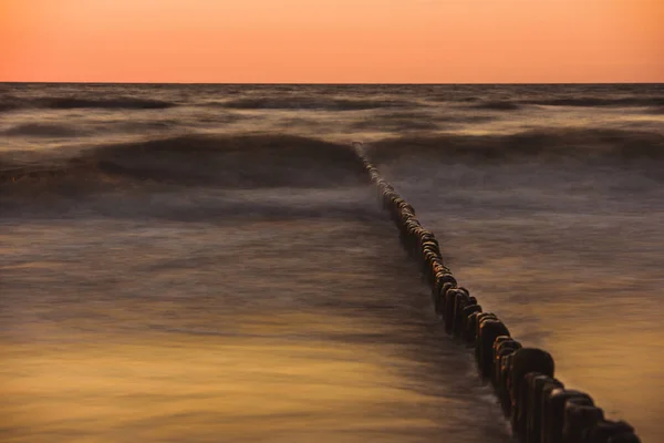 Houten golfbreker bij zonsondergang aan de Baltische Zee — Stockfoto