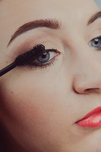 Skönhet modell tonårig flicka tittar i spegeln och tillämpa mascara gör. Vacker ung kvinna applicera makeup — Stockfoto