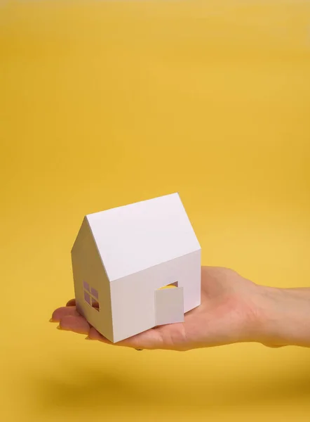 Witte familie papieren huis in de hand van de mens op gele achtergrond papier. Minimalistische stijl. Begrepen, ruimte. Zicht van bovenaf. Verticale oriëntatie. — Stockfoto