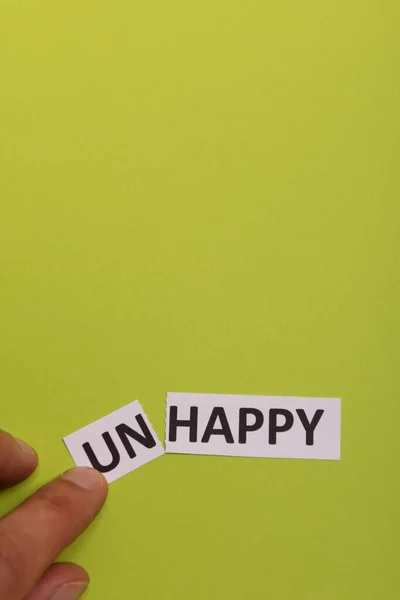 Рука людини тримає листівку з текстом нещасливим, вирізаючи слово "не", так що він написав "щасливий". Копіювати простір. Вапняний фон. Студійна стрілянина — стокове фото