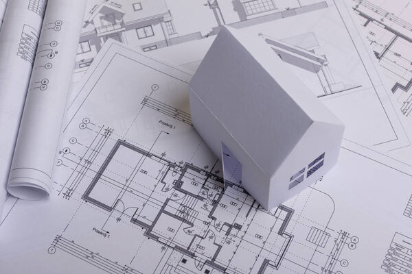White family paper house, house projects plan and blueprints in the background. Minimalistic and simple concept, style. Horizontal orientation.