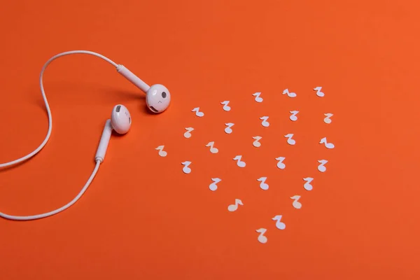 white earphones and white paper notes on orange background. view from above
