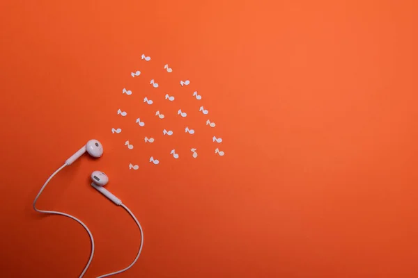 white earphones and white paper notes on orange background. view from above