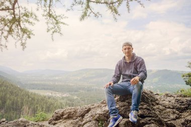 Erkek sırt çantalı dinleniyor ve güneşin altında kayaların üzerinde oturuyor..