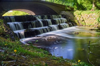 Poznan kentinde bir parkta küçük bir nehir üzerinde köprü ve su eşik