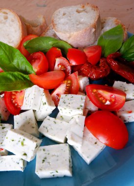 Taze keçi peyniri, domates, fesleğen ve mavi tabakta beyaz ekmek