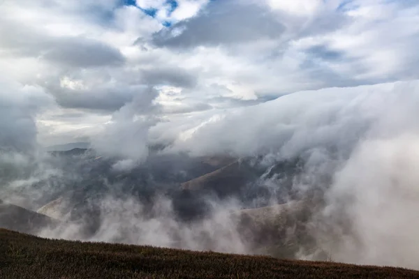 Dramatic rainy alpine landscape with rain clouds below the mountain. Bad autumn weather.