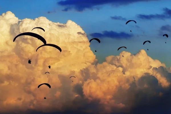 Gaggle of paragliders fly with giant clouds on the background. Paragliding competition