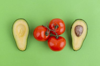 Avokado ve domates yeşil arka plan üzerinde kesti. Sağlıklı yemek malzemeler. 