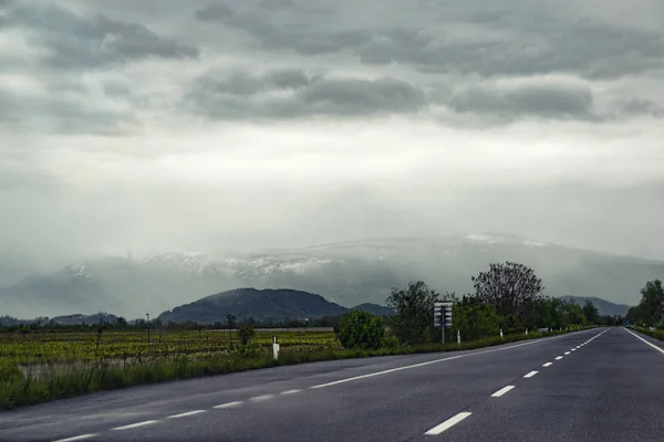 Asfaltväg med regnmoln, snö och berg vid horisonten — Stockfoto