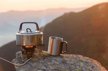 Dağların tepesinde kaynatılmış çay demliği ve metal bardak. Vahşi doğada harika bir akşam.