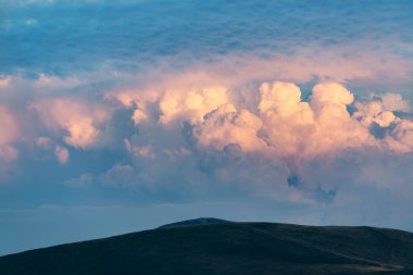 Güçlü fırtına bulutları dağların tepesinde akşam güneşiyle aydınlanıyor.