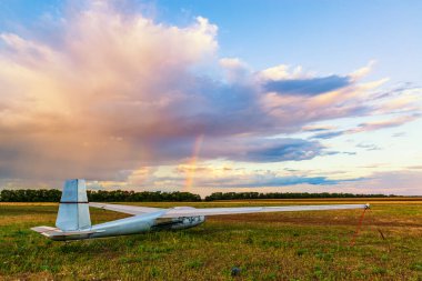 Plane on the airfield with beautiful cloud and rainbow. Sailplane or glider at the airfield is waiting for the adventure.  clipart