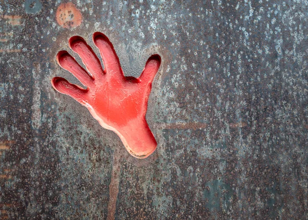 red imprint of a hand on a rusty metal plate