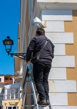 Zanaatkar, İtalya 'da Sardunya' da bir evin ön cephesindeki lambayı tamir ediyor.