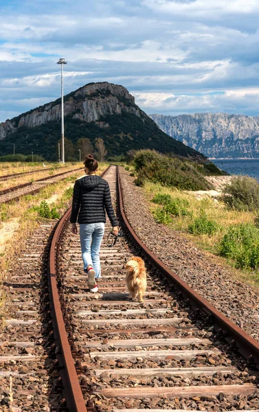 Μια νεαρή γυναίκα περπατάει με το σκύλο της σε ένα παλιό κρεβάτι στίβου, Φιγκαρί, Golfo Aranci, Σαρδηνία, Ιταλία — Φωτογραφία Αρχείου