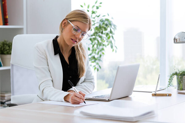 Shot of beautiful young businesswoman writing and reviewing papers in the office.