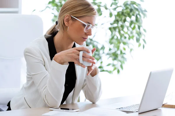 オフィスで彼女のラップトップで作業しながらコーヒーを飲む若い女性実業家のショット — ストック写真